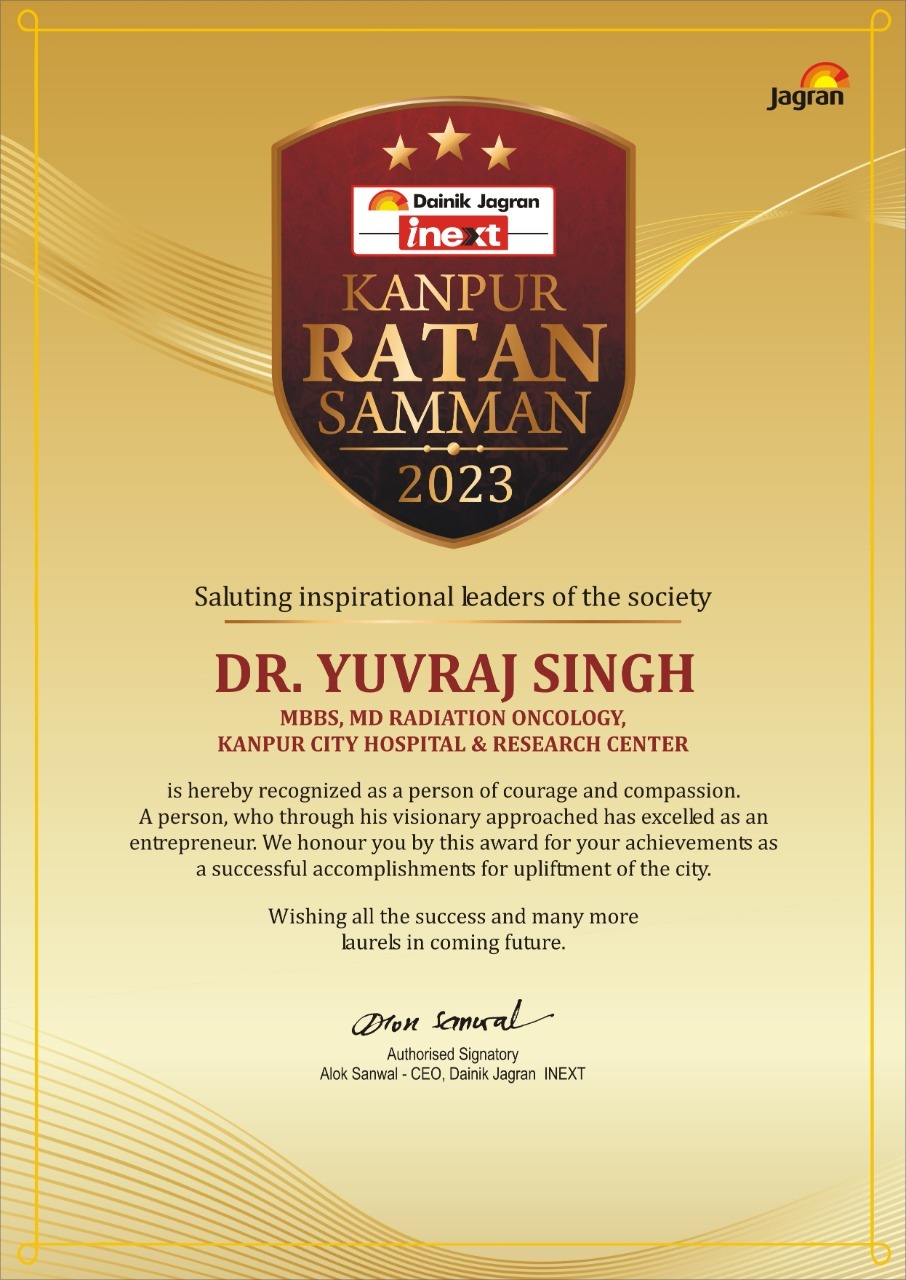 The image shows an official award certificate titled “Kanpur Ratan Samman 2023,” presented by Dainik Jagran iNext. It recognizes Dr. Yuvraj Singh, MBBS, MD Radiation Oncology, from Kanpur City Hospital & Research Center for his courage, compassion, and contributions to society. The certificate features a golden background, a maroon shield emblem with stars, and a message appreciating his achievements, signed by Alok Sanwal, CEO of Dainik Jagran iNext.